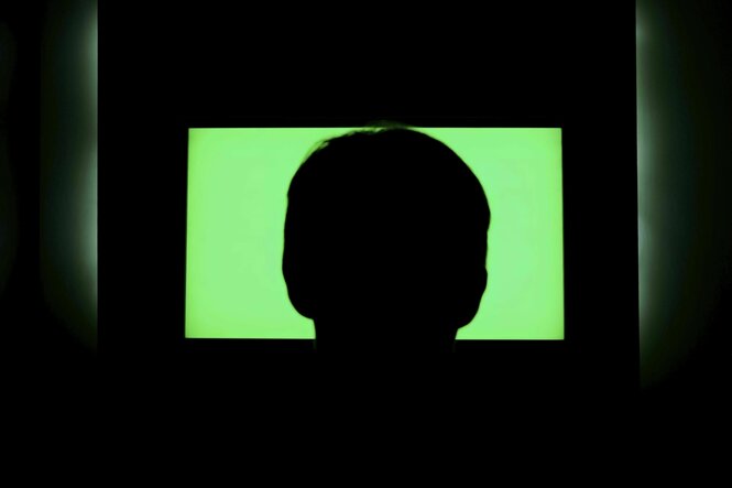 Rückansicht einer Person, die im Dunkeln vor einem Fernseher sitzt