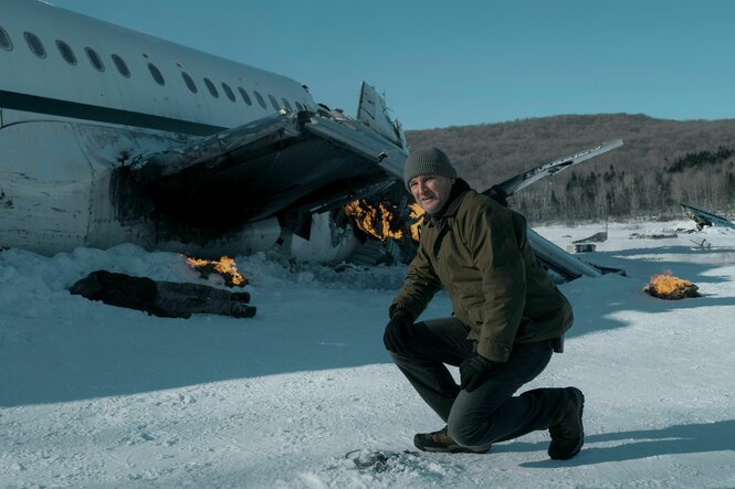 Ein Mann kniet im Schnee vor einem brennenden Flugzeugwrack