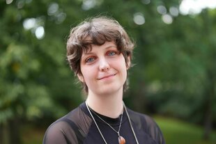 Die Autorin Fiona Sironic, im Hintergrund sommerlich begrünte Bäume