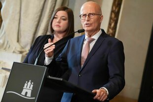 Ein Mann steht an einem Rednerpult. Eine Frau steht bedröppelt dahinter