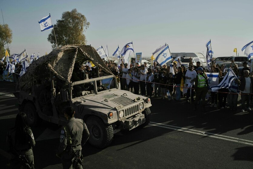 Menschen schwenken israelische Flaggen, als ein Militärfahrzeug vor der Ankunft eines Konvois mit aus dem Gazastreifen befreiten Geiseln auf einem Militärstützpunkt in der Nähe von Reim im Süden Israels vorbeifährt.