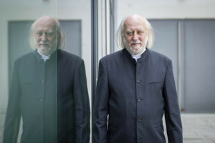 Zu sehen ist der Schriftsteller László Krasznahorkai, rechts neben einem spiegelnden Fenster.