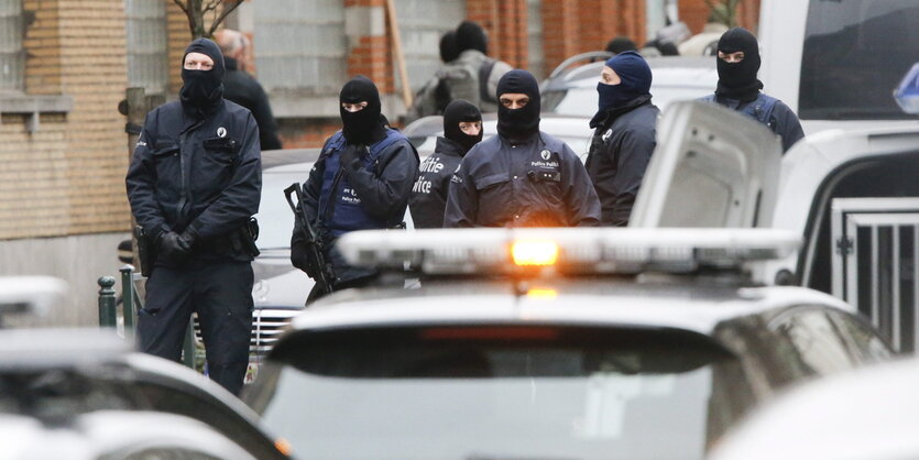 Vermummte Polizisten in einer Straße in Molenbeek, im Vordergrund Autos.