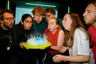 Mehrere Personen pusten Kerzen auf einer Torte aus