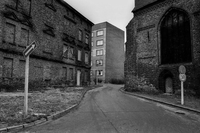 Schwarz-weiß-Foto von einer Straße, alte Gemäuer, im Hintergrund ein Plattenbau