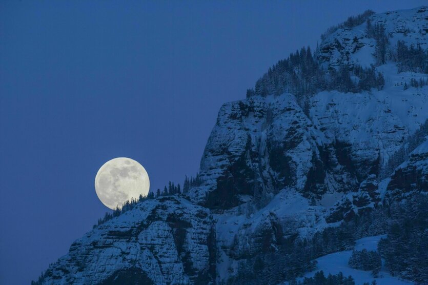 Ein Berg im Schnee, dahinter der Vollmond, das Bild ist in Blau getaucht