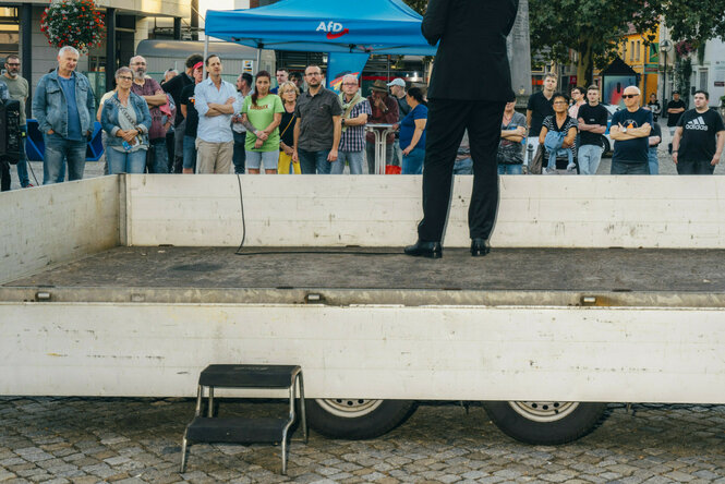 Ein Mann im schwarzen Anzug steht auf einer Rednerbühne. Er ist von hinten zu sehen
