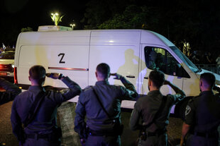 Ein weißer Transporter, im Vordergrund salutierende Soldaten