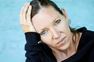 Eine Frau in dunklem Pullover fasst sich an den Kopf