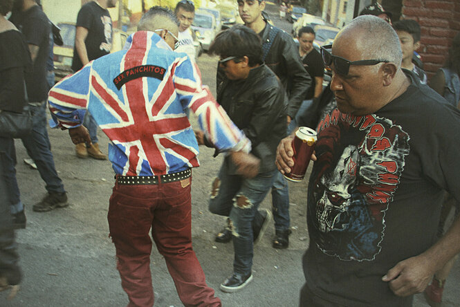 Eine Gruppe Punks tanzt auf einer Straße in Mexiko City. Ein Mann, der in der Mitte des Filmstills mit dem Rücken zur Kamera tanzt, trägt eine Jacke mit dem Muster der britischen Flagge und der Aufschrift "Sex Panchitos".