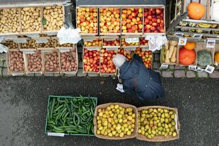 Eine Frau steht auf einem Wochenmarkt an einem Stand mit Obst und Gemüse