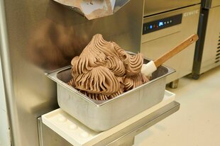Aus einem professionellen Eisgerät wird Schokoladeneis in einen Edelstahlbehälter abgefüllt.