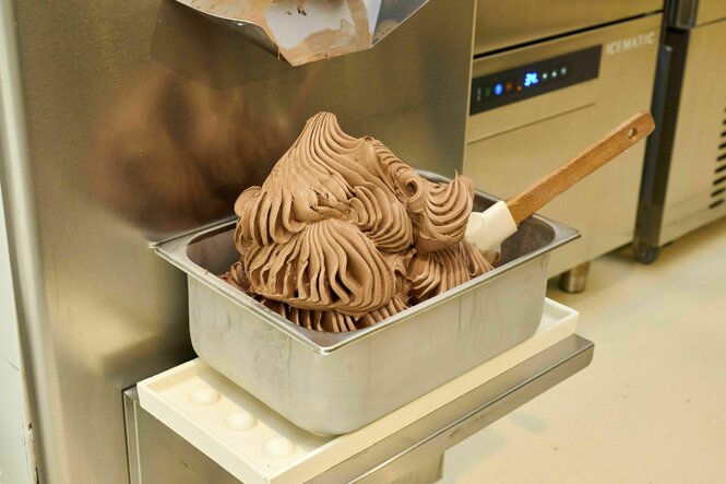 Aus einem professionellen Eisgerät wird Schokoladeneis in einen Edelstahlbehälter abgefüllt.