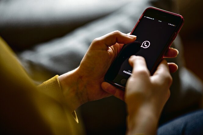 Eine Person hält ein Smartphone. Auf dem Display ist das Logo von Whatsapp zu sehen.