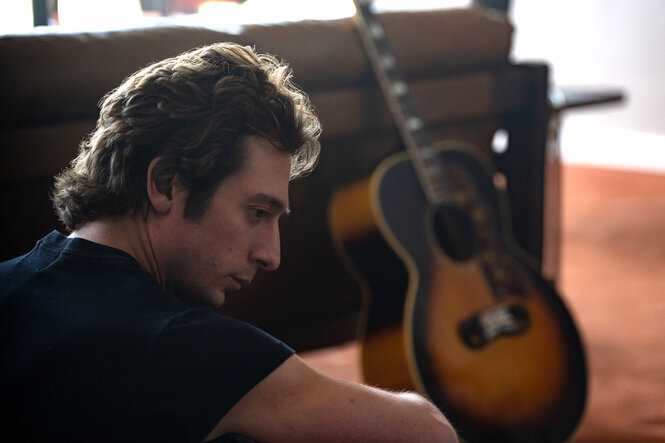 Der "Boss" (Jeremy Allen Walker) sitzt im Wohnzimmer auf dem Boden, im Hintergrund eine Gitarre.