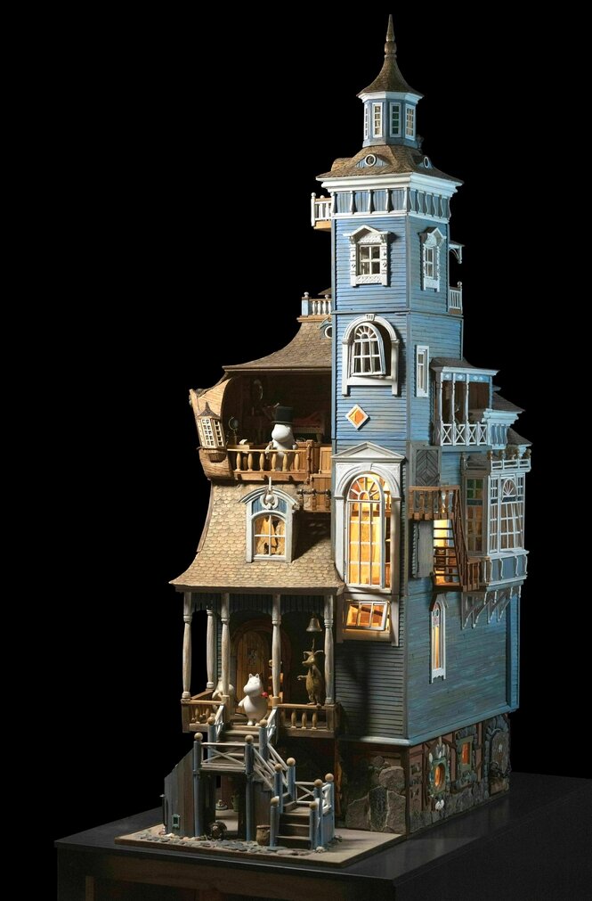 Das Muminhaus - hellblaues Holz mit weissen Fenstern und die Türen immer offen steht auf einem Spielplatz im Sommer umgeben von Bäumen