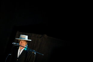 Bob Dylan mit Hut vor einem schwarzen Bühnenhintergrund