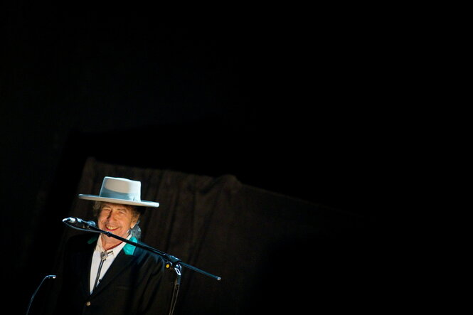 Bob Dylan mit Hut vor einem schwarzen Bühnenhintergrund