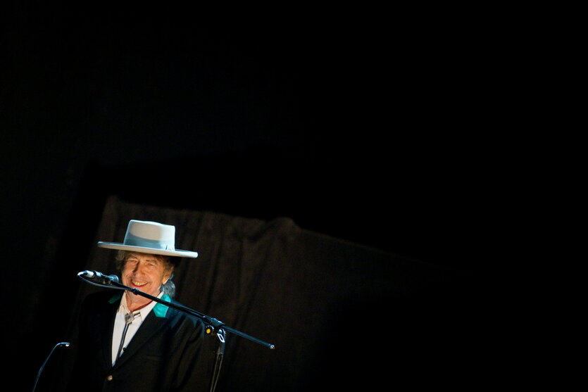 Bob Dylan mit Hut vor einem schwarzen Bühnenhintergrund