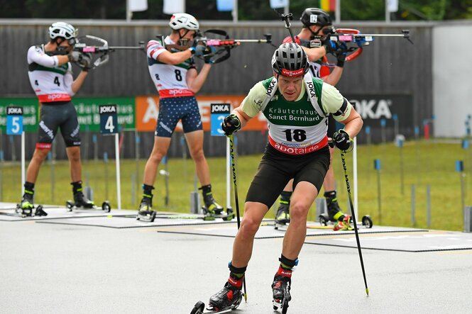 Biathlet auf Rollskiern im Vordergrund, im Hintergrund drei Biathleten am Schießstand