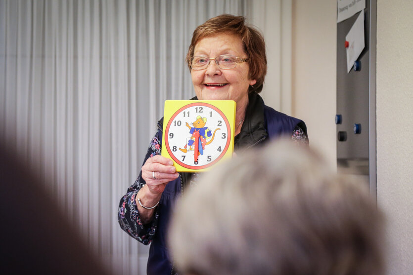 Eine ältere Frau hält eine größere Uhr hoch, auf der eine Maus abgebildet ist