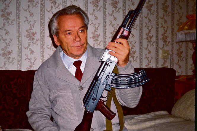 Älterer Herr mit Sturmgewehr AK-47 in einem bürgerlichen Wohnzimmer.