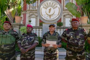 Vier Männer in Militäruniformen stehen vor dem Wappen der Republik Madagaskar. Im Hintergrund der Präsidentenpalast und Palmen.