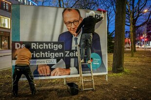 Zwei Personen kleben ein Wahlplakat auf eine Stellwand