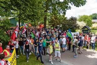 Demonstrierende mit Fahnen und Bannern stehen unter Bäumen in Brettorf