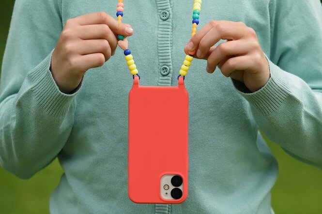 Kinderhände halten ein rotes Smartphone an einer bunten Kette