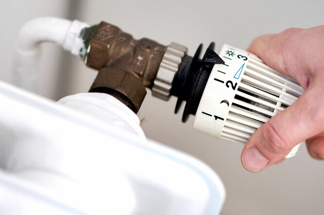 Eine Frau dreht am Thermostat einer Heizung