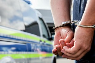 Einen Person steht in Handschellen gefesselt neben einem Polizeifahrzeug