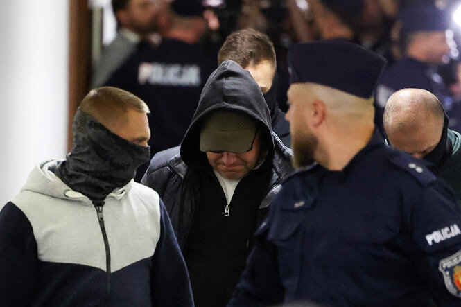Ein Mann, der sein Gesicht mit Mütze und Kapuze verdeckt, umringt von Polizisten