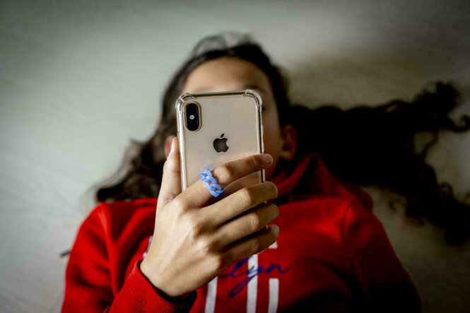Junges Mädchen liegt auf dem Rücken mit einem Smartphone in der Hand, sie trägt ein rotes Shirt