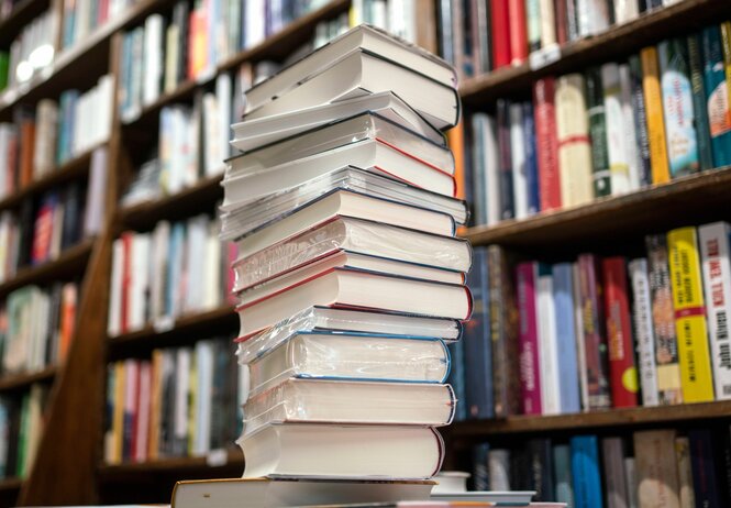 Das Foto zeigt einen Bücherstapel vor einem Bücherregal.