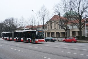 Ein Bus fährt an einem Gebäude mit Säulen-Eingang vorbei