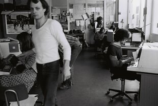 Schwarzweißfoto von einem Büro, ein junger Uli Küsters im weißen T-Shirt läuft durchs Bild