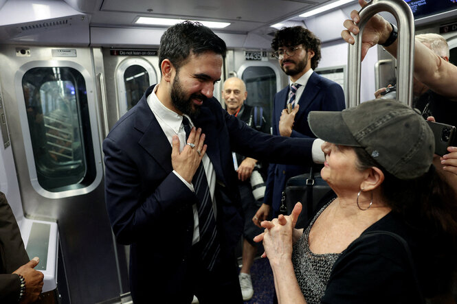 Zohran Mamdani spricht mit einer Frau während einer U-Bahnfahrt