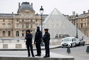 Drei Polizisten stehen vor der Glaspyramide, die den Eingang zum Louvre bildet