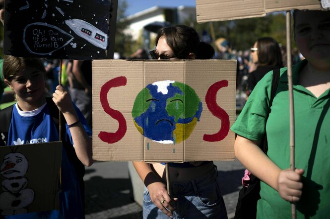 Demonstriende mit Schild: Darauf gemalt eine Erde, die das O in SOS bildet