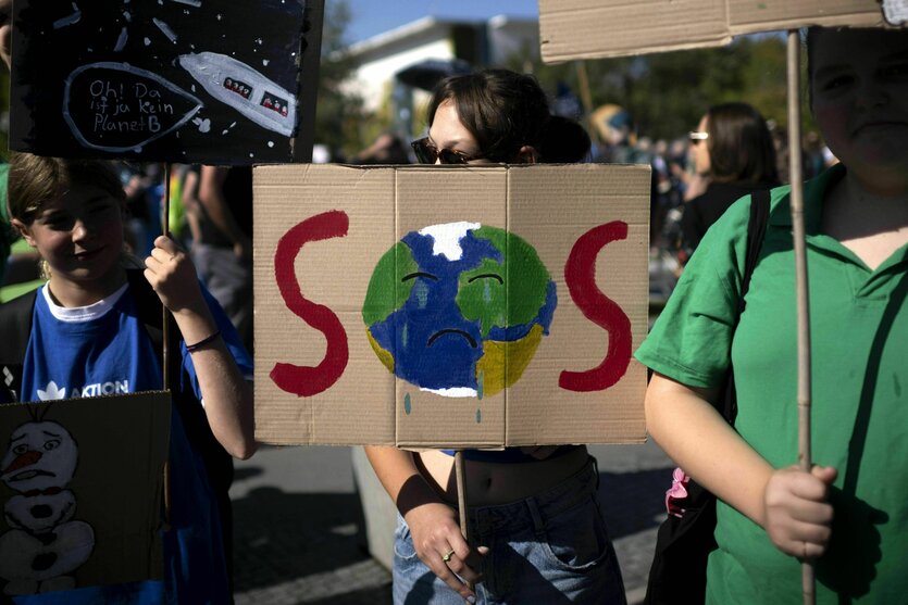 Demonstriende mit Schild: Darauf gemalt eine Erde, die das O in SOS bildet