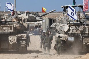 Menschen stehen zwischen zwei Panzern mit aufgesteckten israelischen Flaggen stehen in einem wüstenähnlichen Gebiet