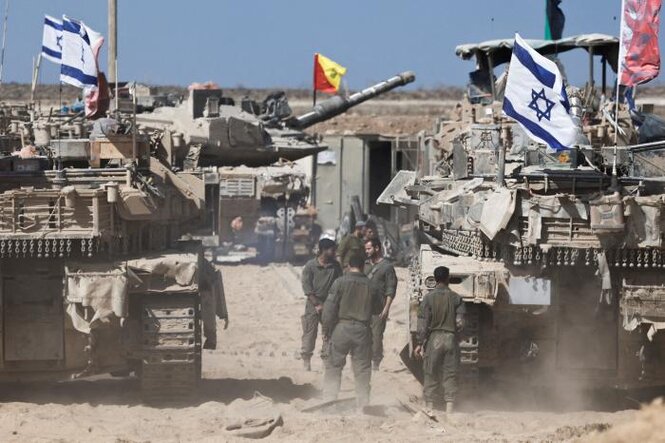 Menschen stehen zwischen zwei Panzern mit aufgesteckten israelischen Flaggen stehen in einem wüstenähnlichen Gebiet