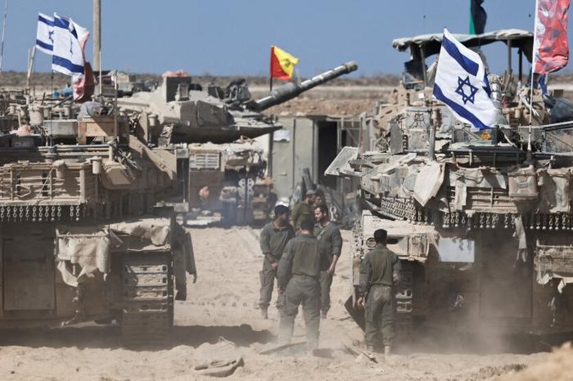 Menschen stehen zwischen zwei Panzern mit aufgesteckten israelischen Flaggen stehen in einem wüstenähnlichen Gebiet