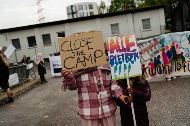 Zwei Menschen halten Schilder mit der Aufschrift "Close the Camp" und "Alle bleiben"