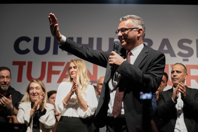 Tufan Erhürman mit Mikrofon winkt in die Menge, im Hintergrund applaudierende Anhänger:innen