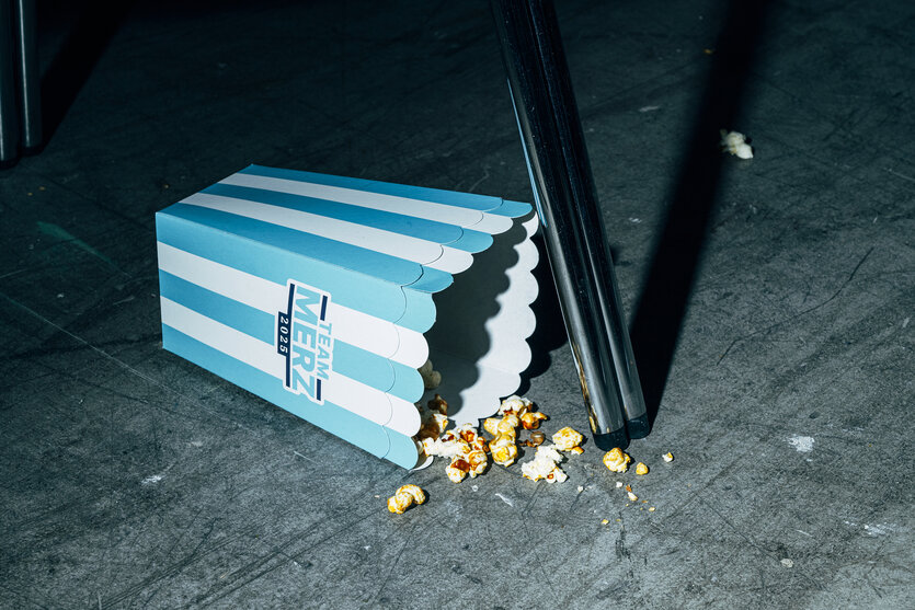 Eine halbleere Pappschachtel Popcorn liegt neben einem Stuhlbein auf dem Boden