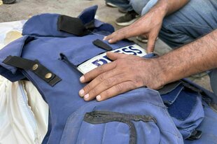 Ein Leichnam ist mit einer Presse-Weste bedeckt, die Hände eines Mannes liegen darauf