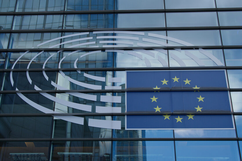 An der gläsernen Fassade des Europäischen Parlaments ist das EU-Logo und die EU-Flagge zu sehen