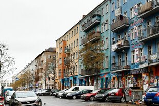 Die Rigaer Straße ist zu sehen. Transparente hängen von dem Haus an der Rigaer Straße 94. Davor stehen Autos.